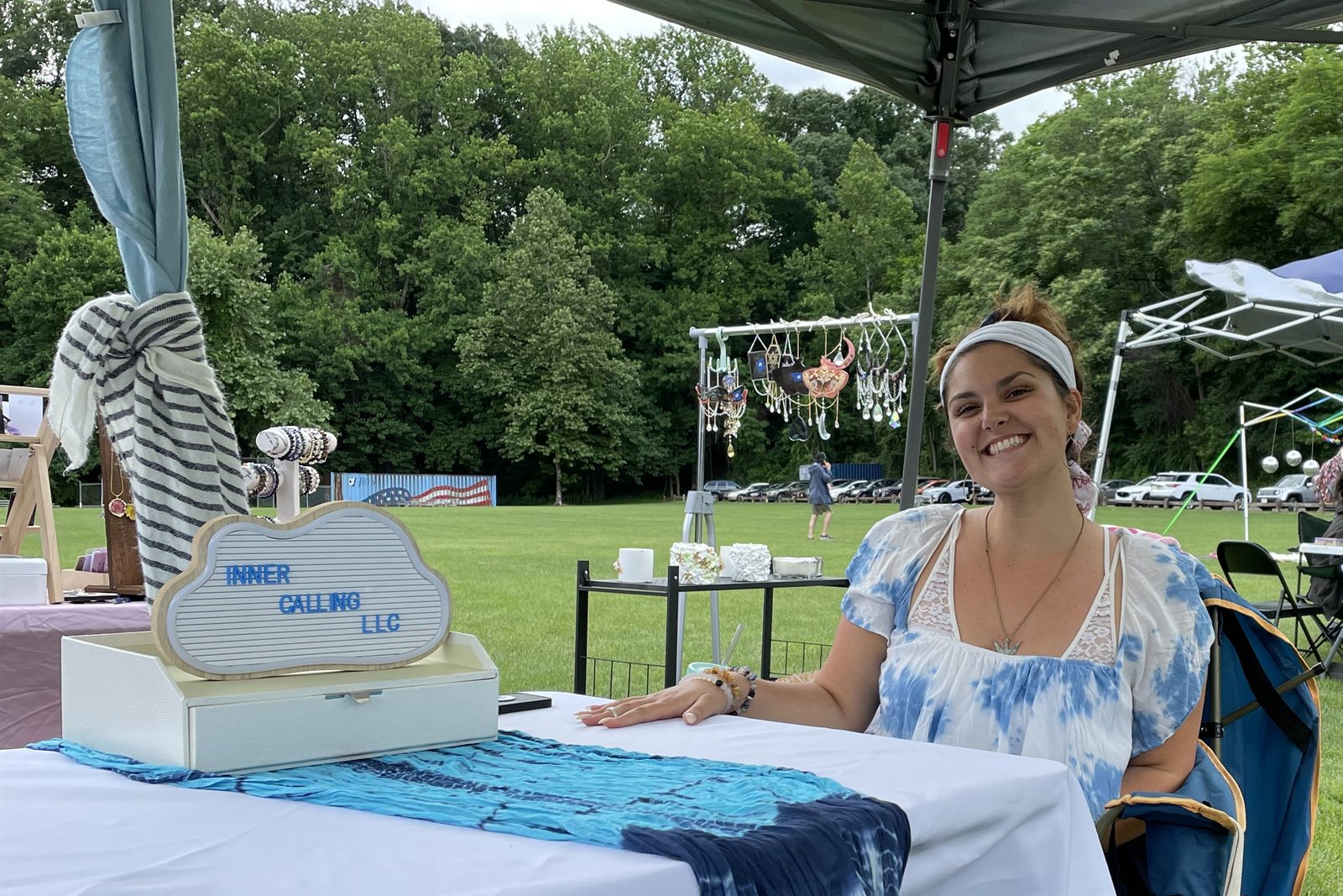 Amanda smiling at her table under a canopy at an outdoor market, an Inner Calling LLC letterboard sign beside her