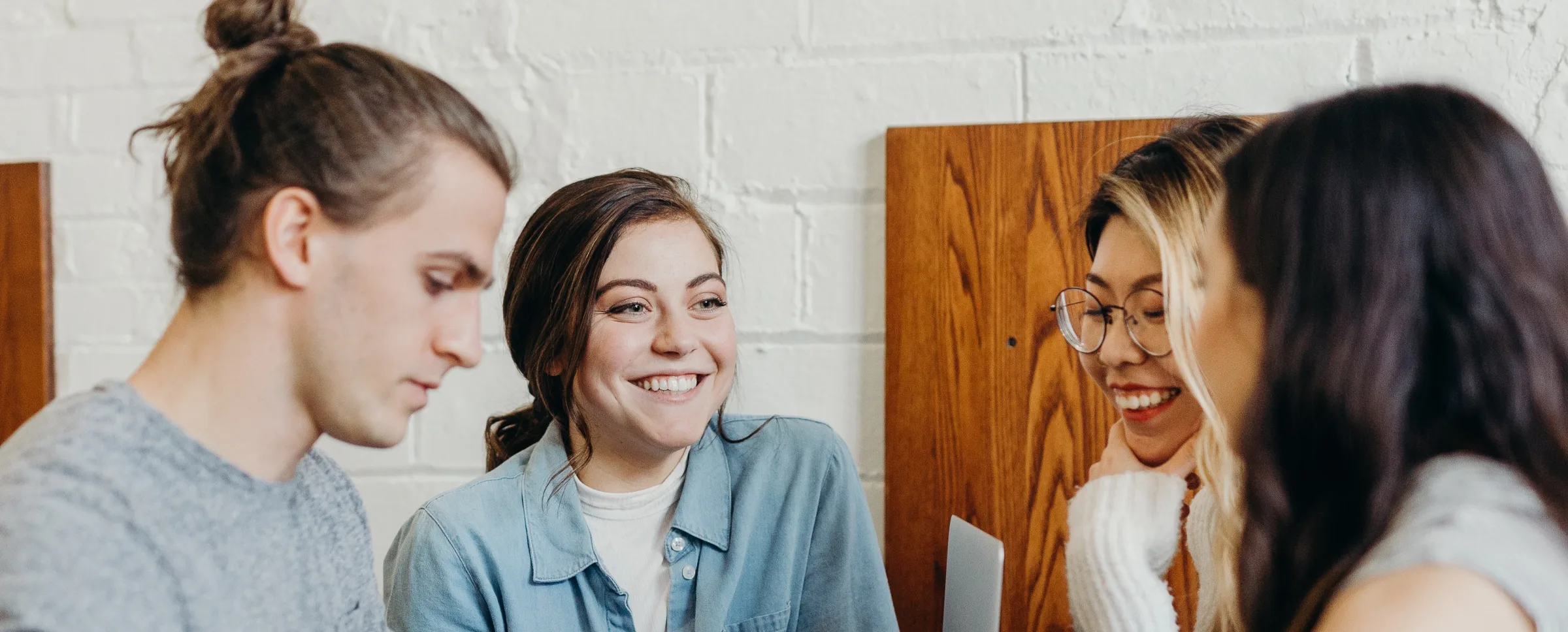 4 people standing and sitting near the table and looking at a laptop