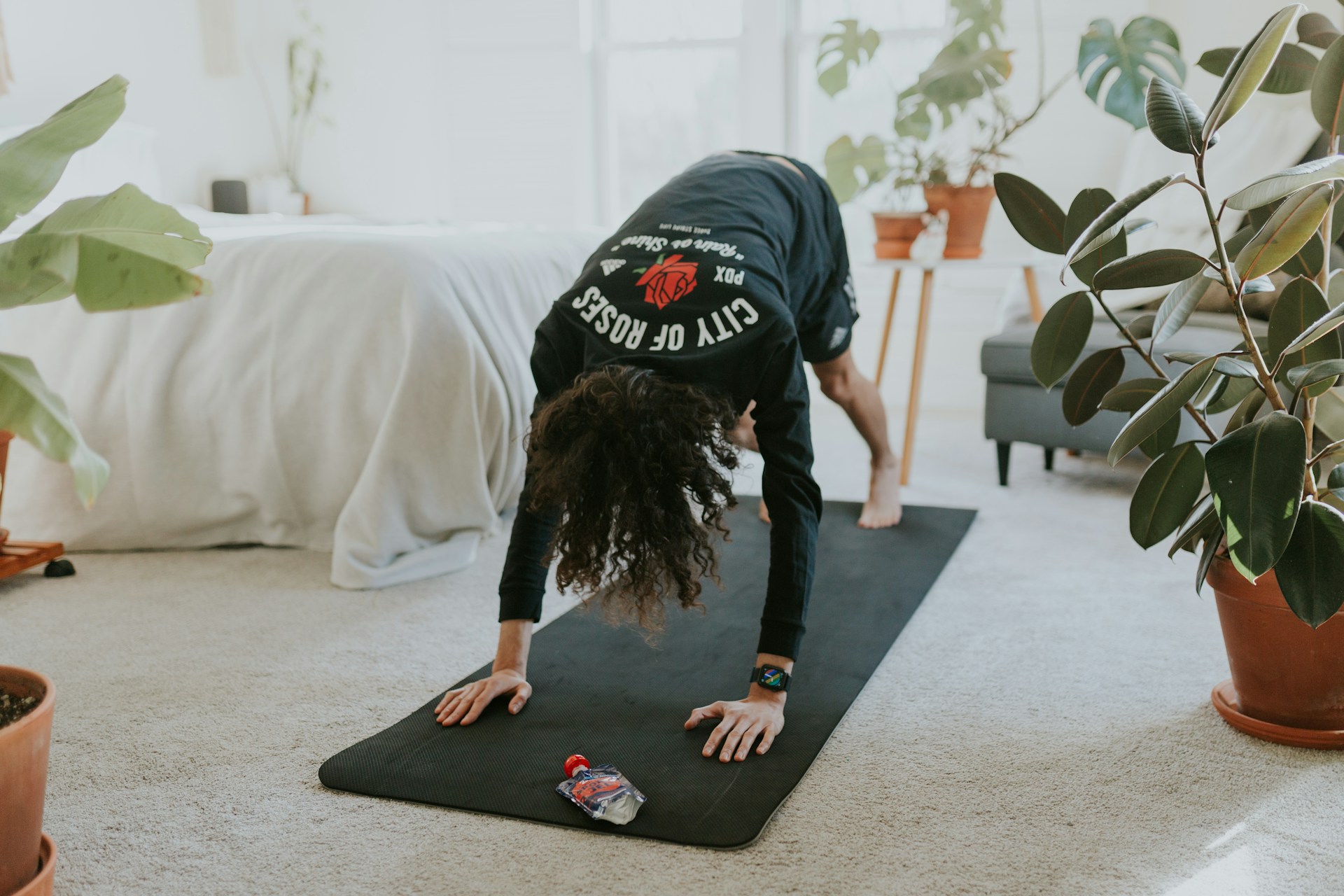A person practices yoga on a mat in a bright, plant-filled home space.