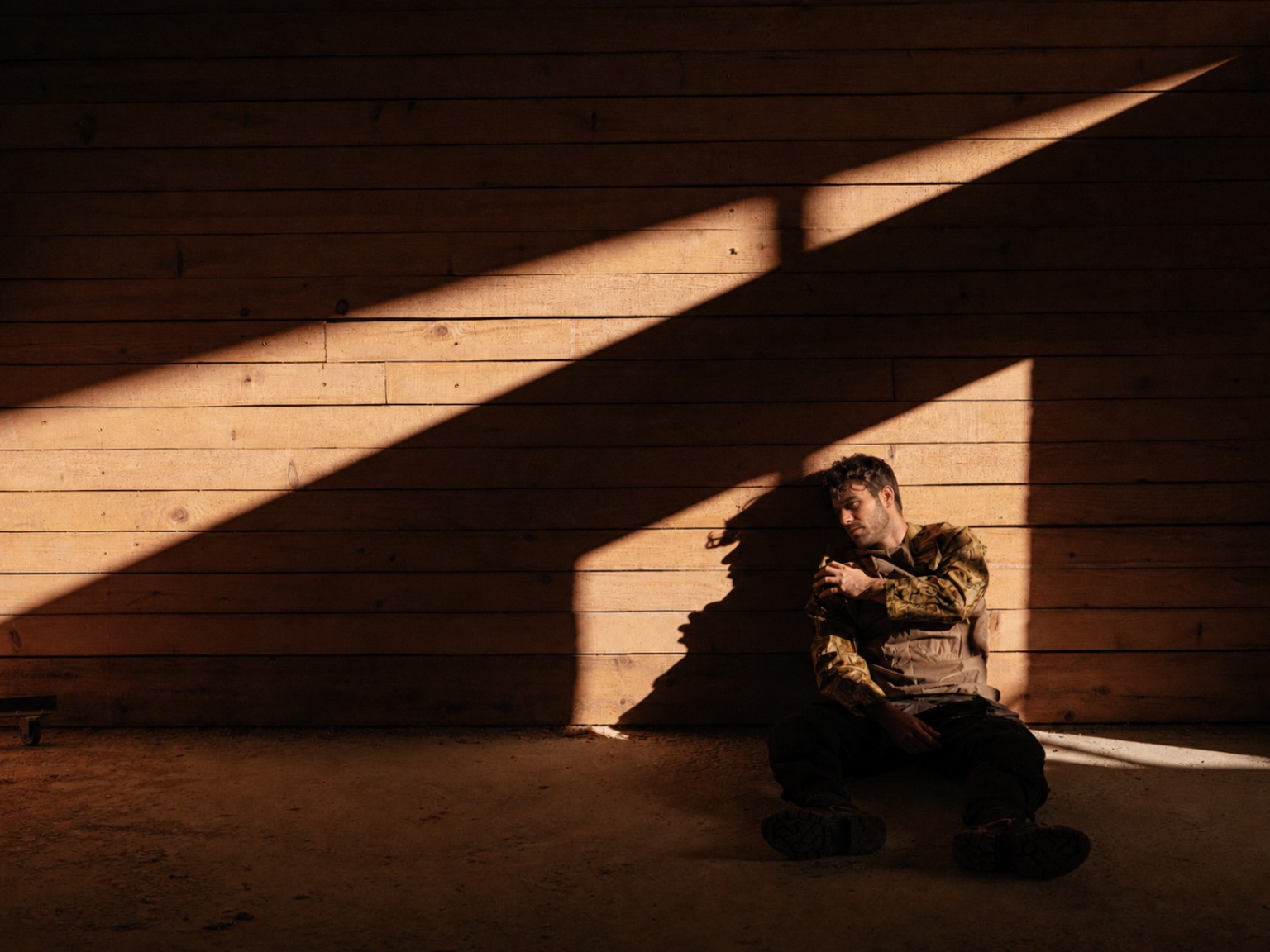 Person seated against a sunlit timber wall.