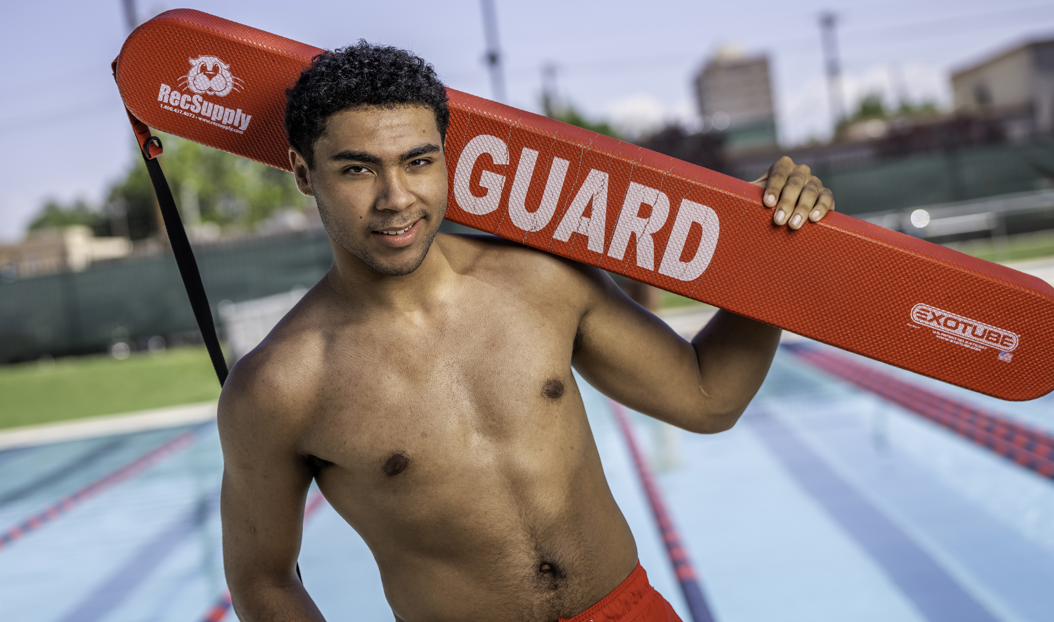 Lifeguard holding a red rescue tube beside a swimming pool