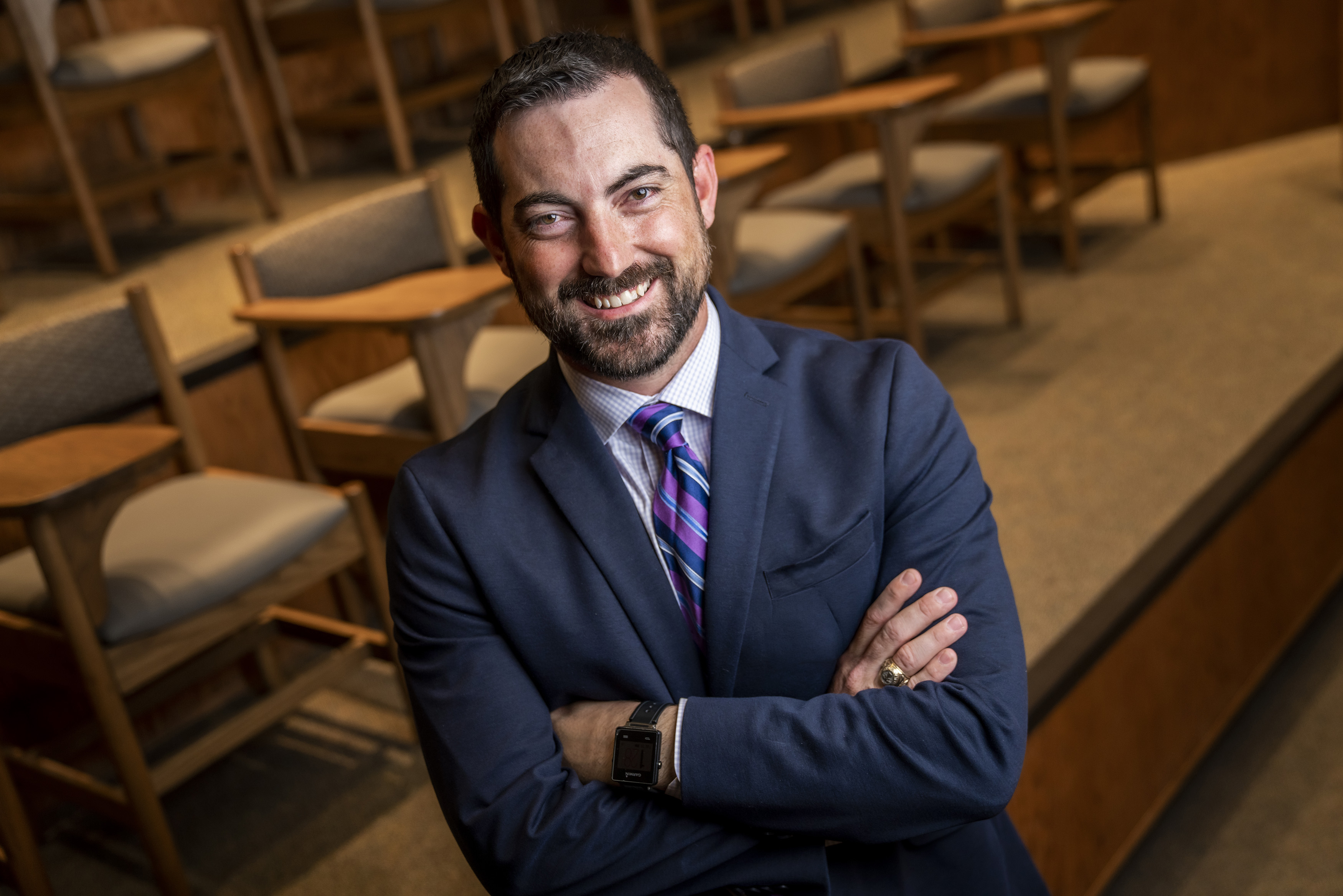 Man in a suit smiling with arms crossed in an auditorium