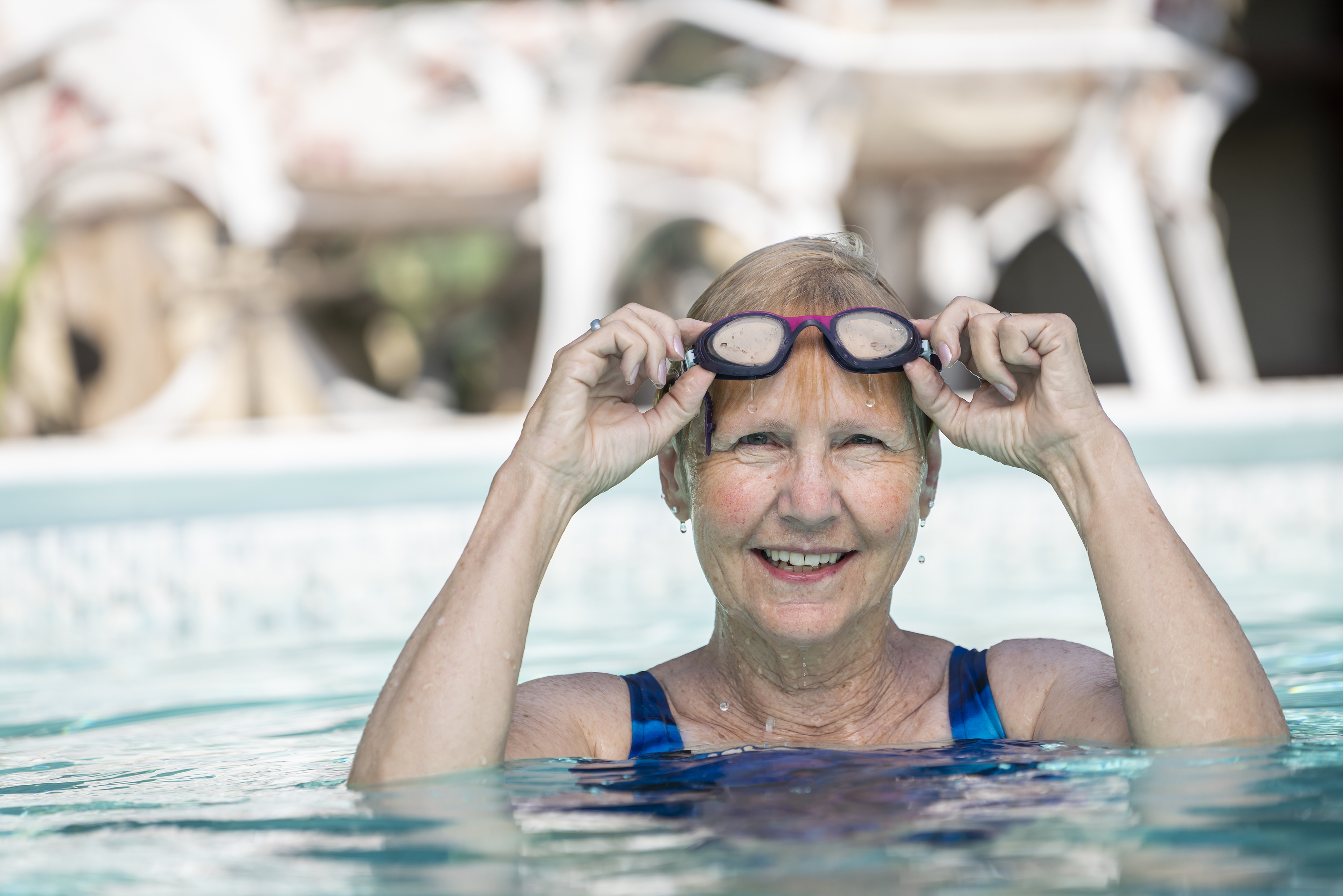 Woman in a swimming pool lifting goggles onto her forehead