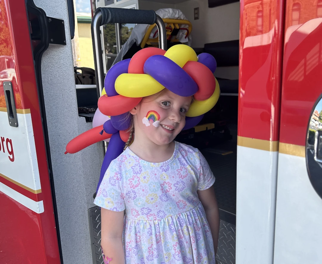 child with a rainbow facepaint and balloon hat