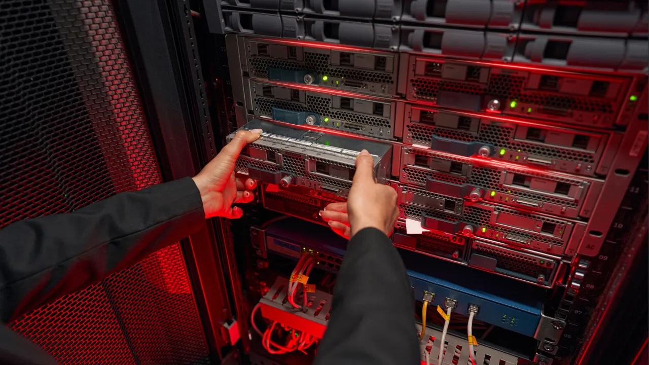 Profissional realizando manutenção em servidor dedicado dentro de um data center, com iluminação em tons vermelhos destacando o hardware. A imagem transmite a ideia de controle, infraestrutura robusta e operação técnica de alto nível — contexto ideal para conteúdos sobre cloud e servidores dedicados.