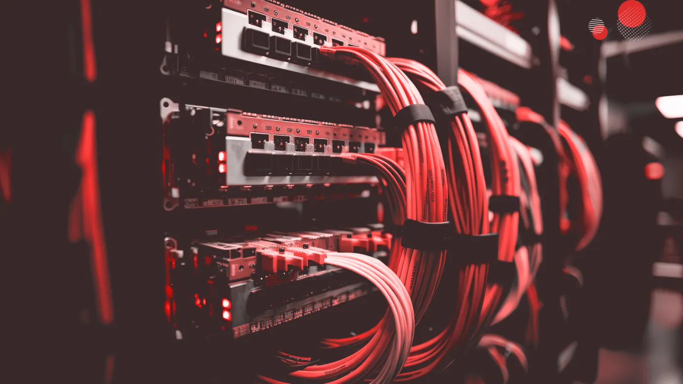 A imagem captura o interior detalhado de um data center, focalizando a estrutura de um rack de servidores com cabos vermelhos organizados meticulosamente. Os componentes iluminados sugerem um ambiente de alta tecnologia e confiabilidade, crucial para operações de "colocation em data center", onde múltiplos clientes alocam equipamento de servidor em uma instalação compartilhada, otimizando a infraestrutura e a conectividade.