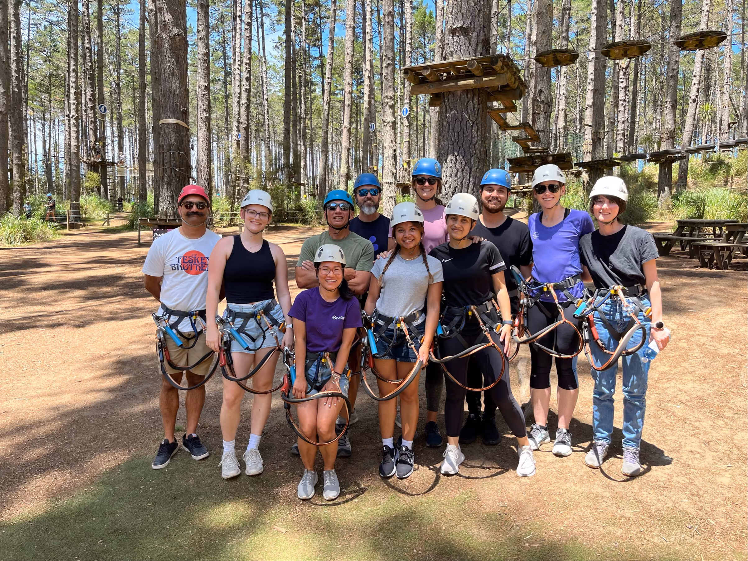 Group of people wearing helmets and harnesses standing in a forest adventure park on a sunny day.