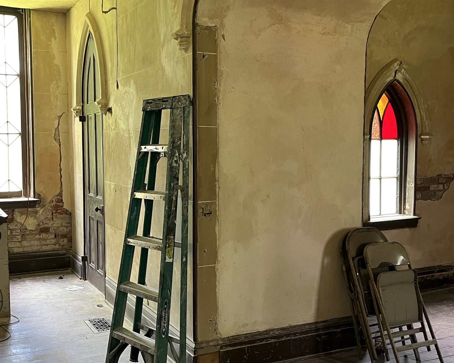 Christ Church sanctuary during restoration with a ladder, exposed walls, and stained glass.