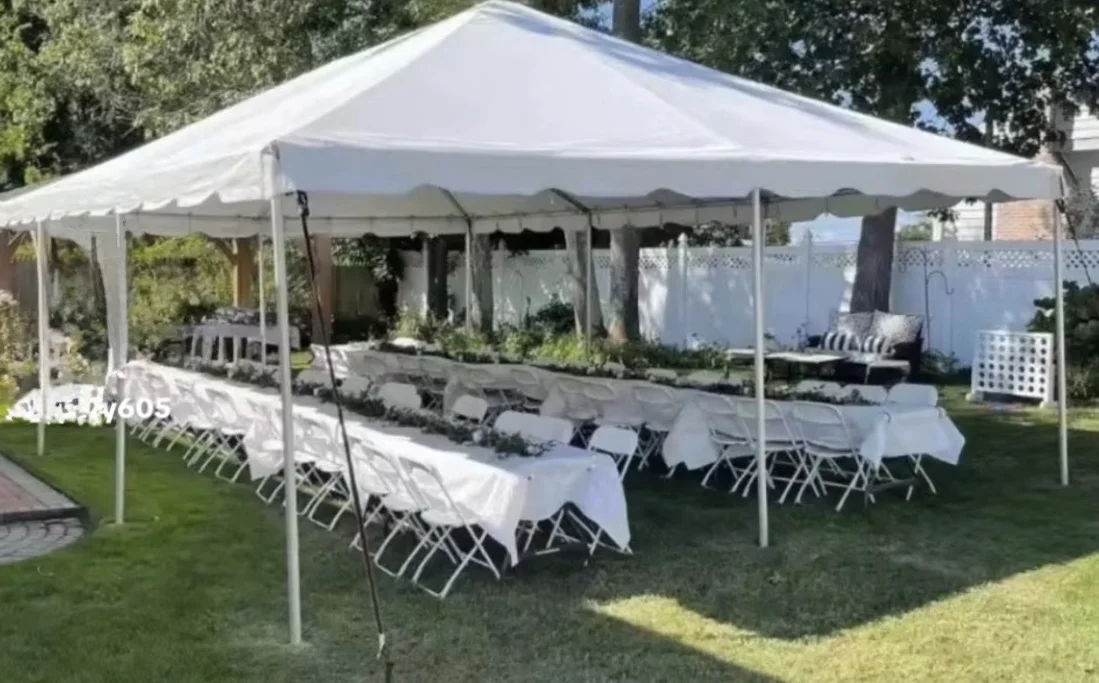 White outdoor canopy over cloth-covered banquet tables and white folding chairs.