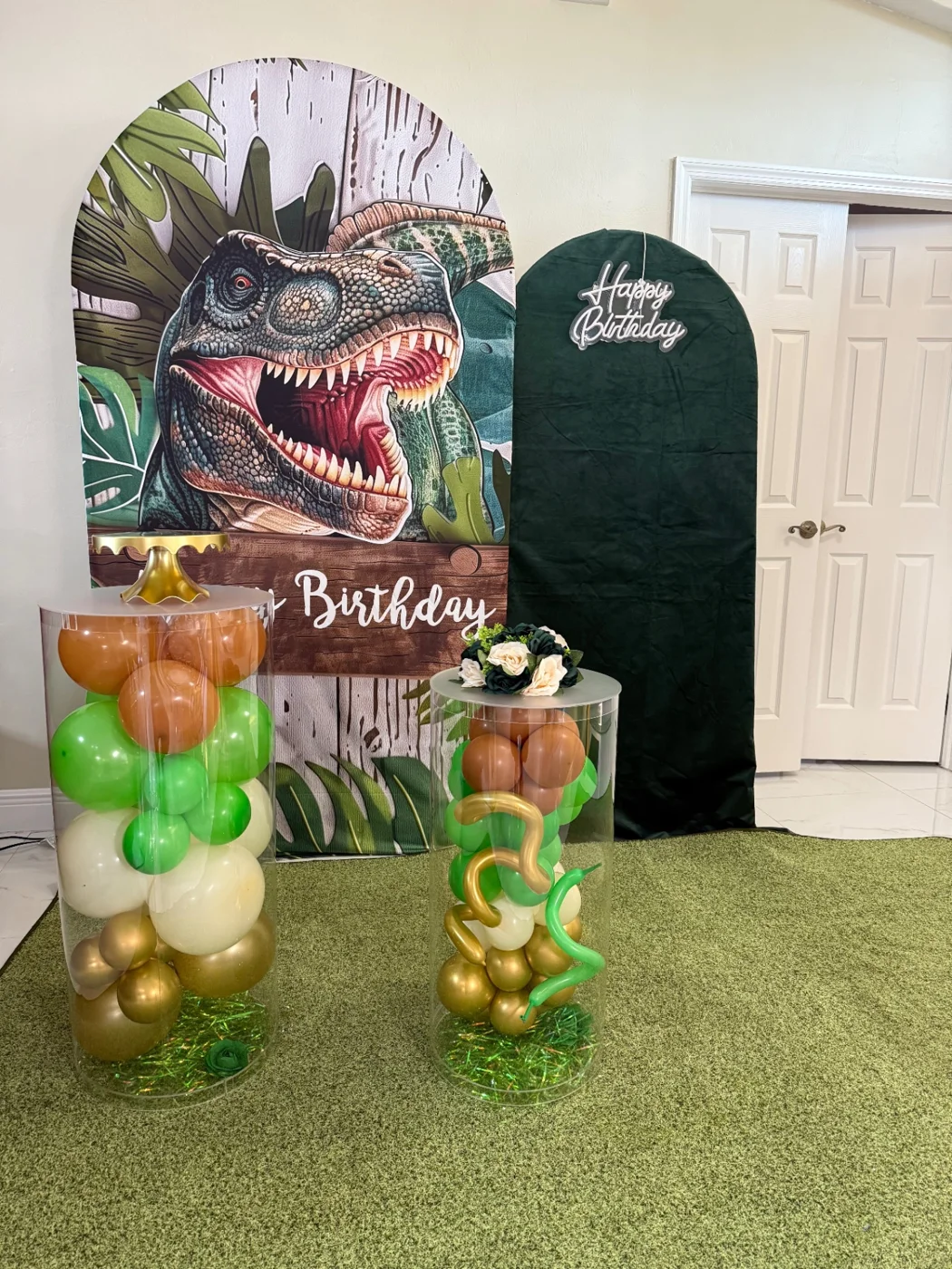 Dinosaur birthday backdrop with dark-green greeting panel and two clear balloon-filled stands.