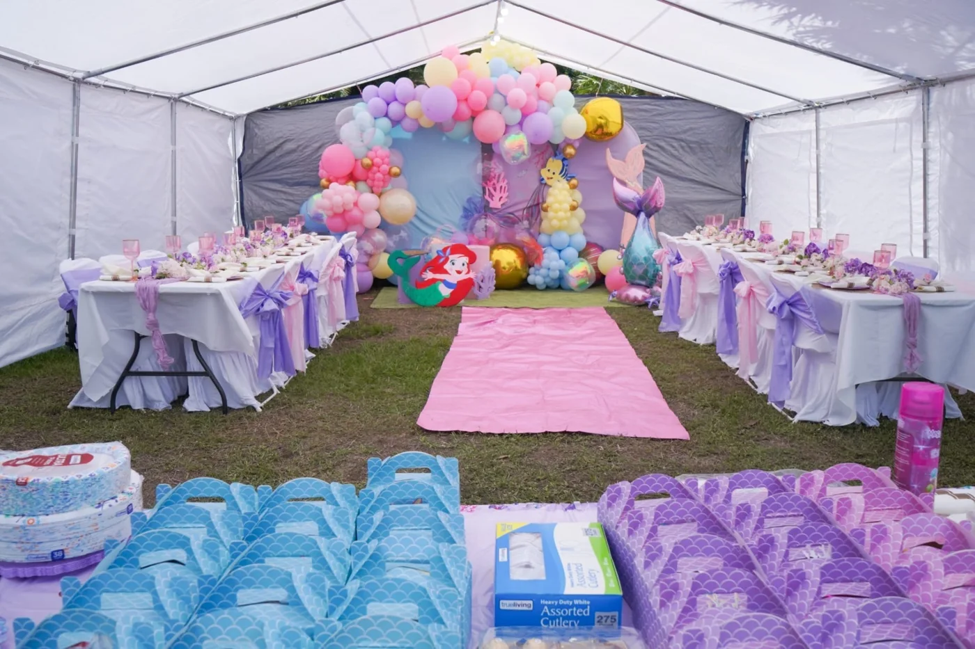White tent with mermaid decorations, pastel table settings, chair bows, pink aisle and patterned favor boxes.
