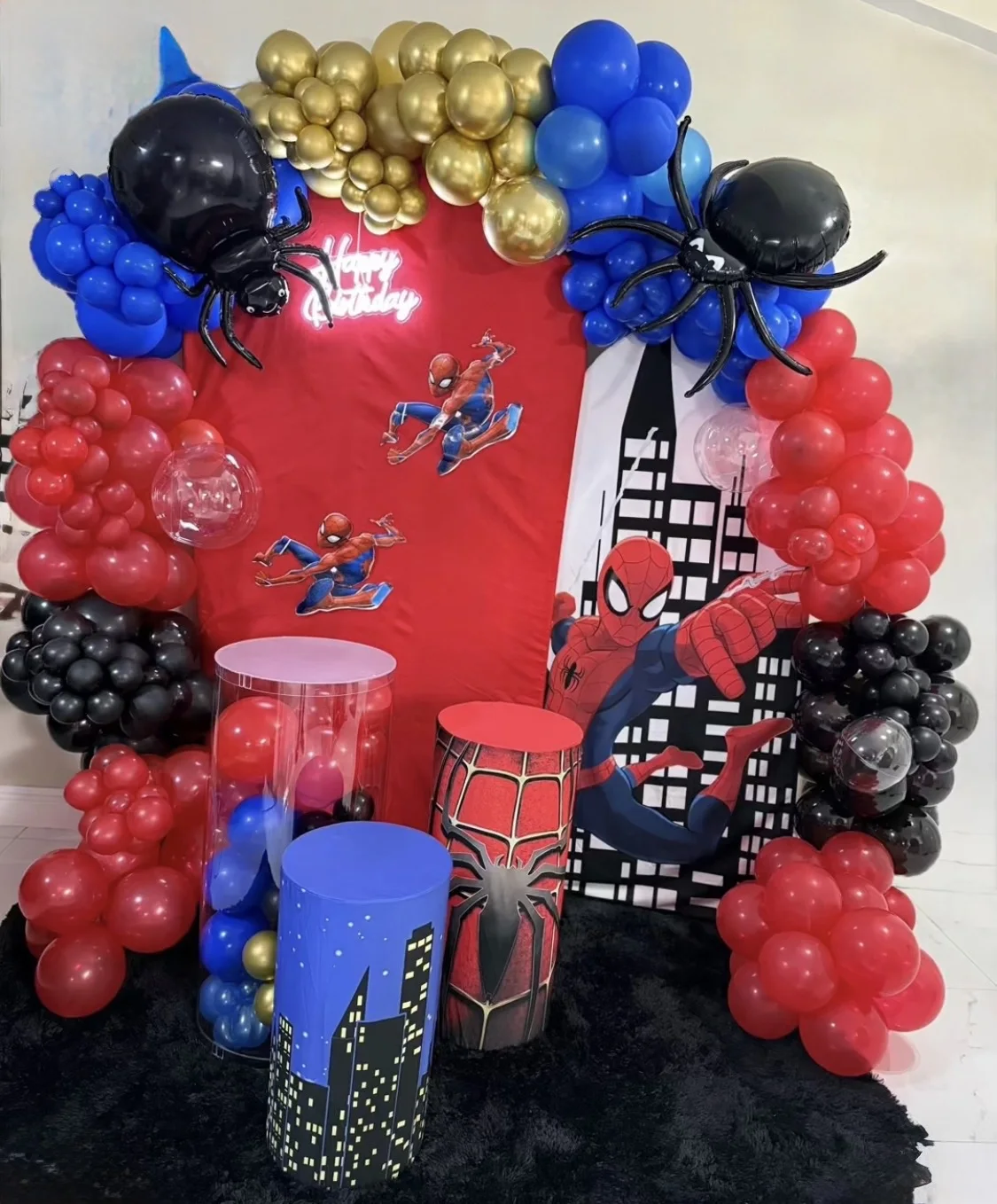 Superhero birthday display with red backdrop, city graphics, balloon spiders and three cylindrical stands.
