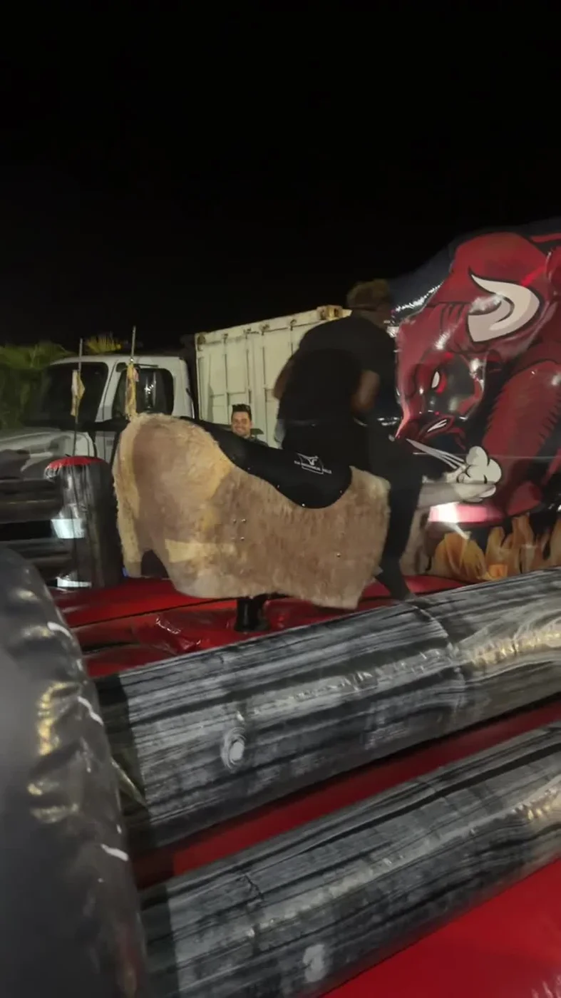 Bull-shaped ride in a red-and-gray enclosure at night with people nearby.
