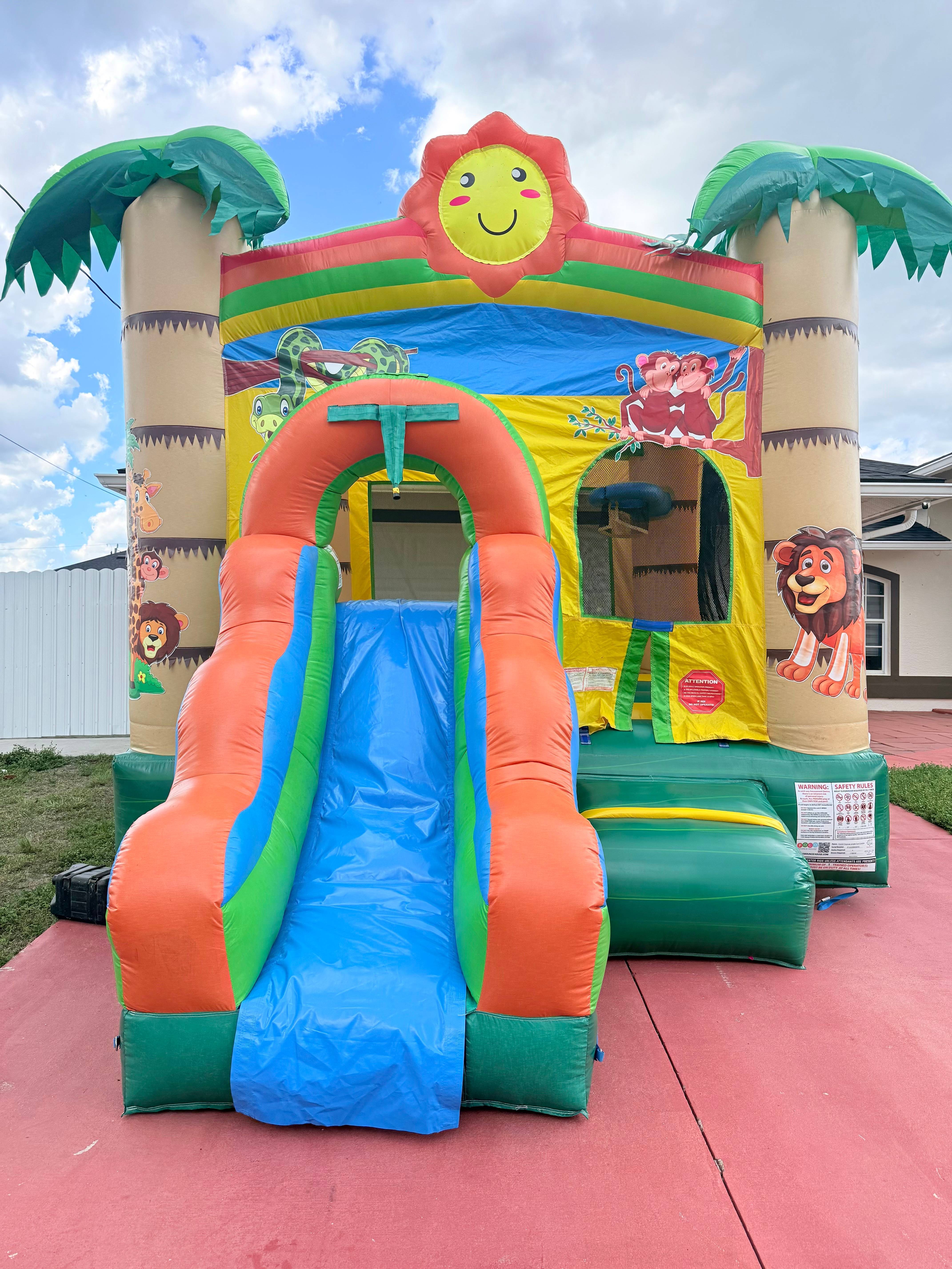 Jungle-themed inflatable bounce house and slide with palm columns and cartoon animals.