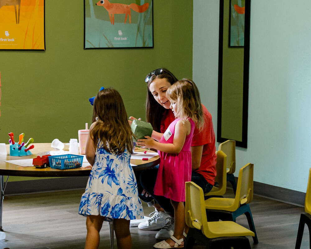 A Waumba Land leader helping two young girls with a craft at a table