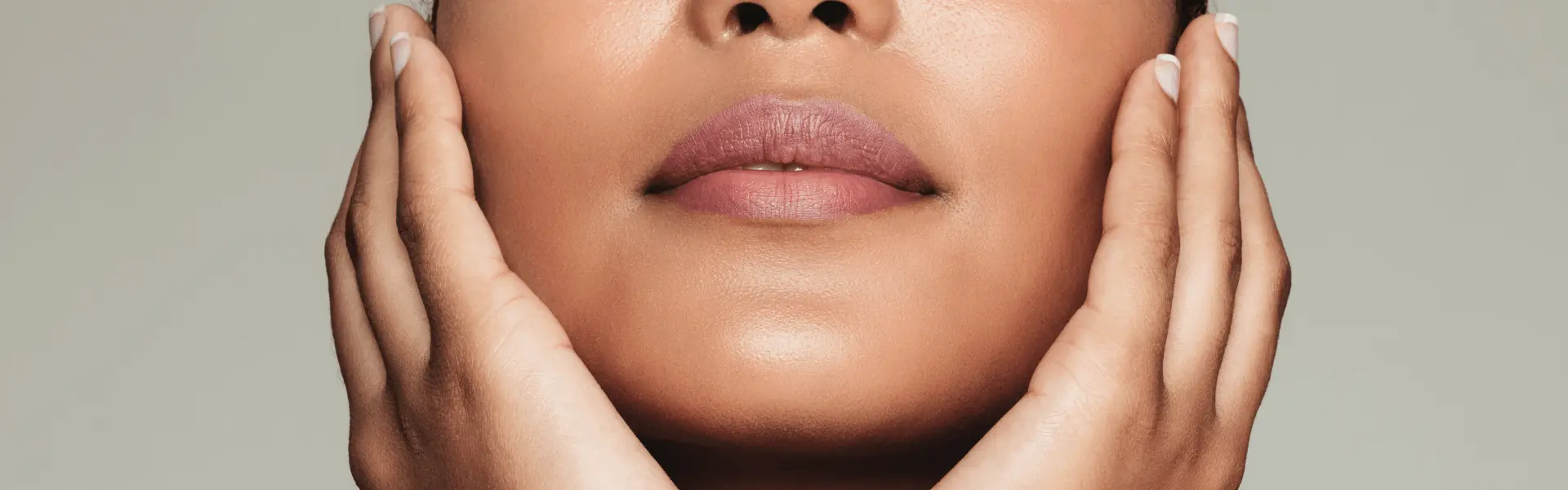 Close-up of a woman's lower face with her hands resting against her cheeks.
