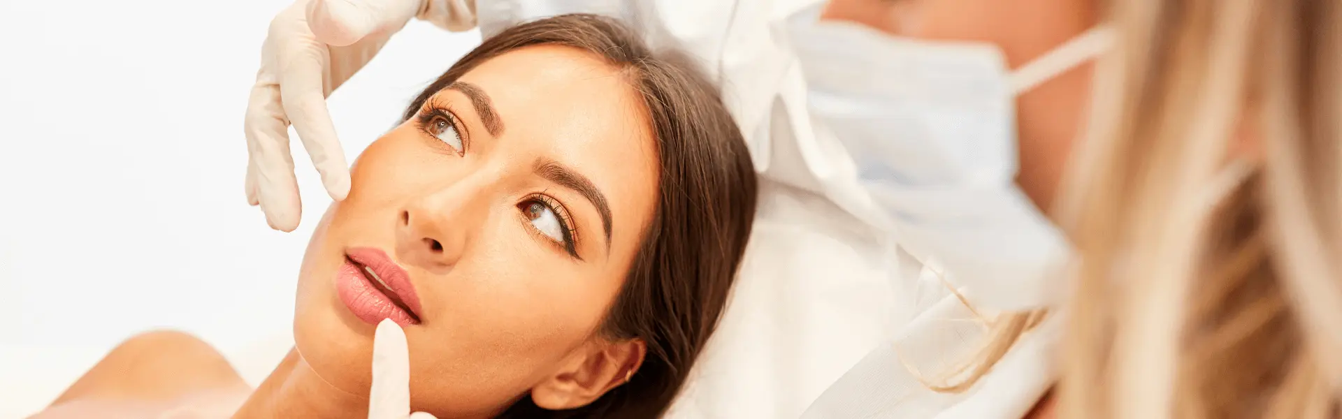 Gloved practitioner examining a woman's face.