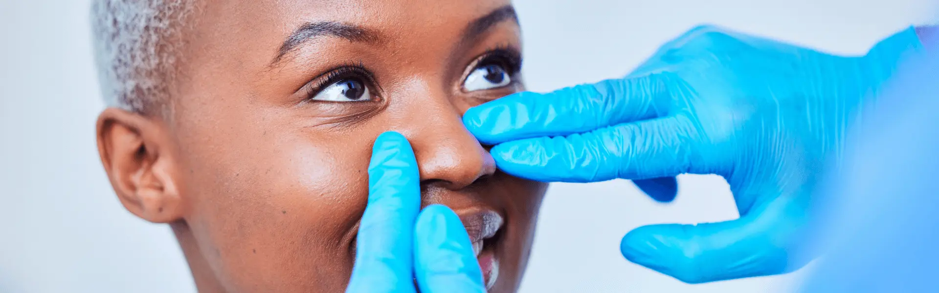 Gloved hands examining a woman's nose.