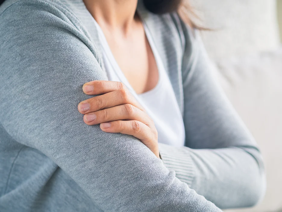 Person in a gray cardigan resting a hand on the opposite upper arm