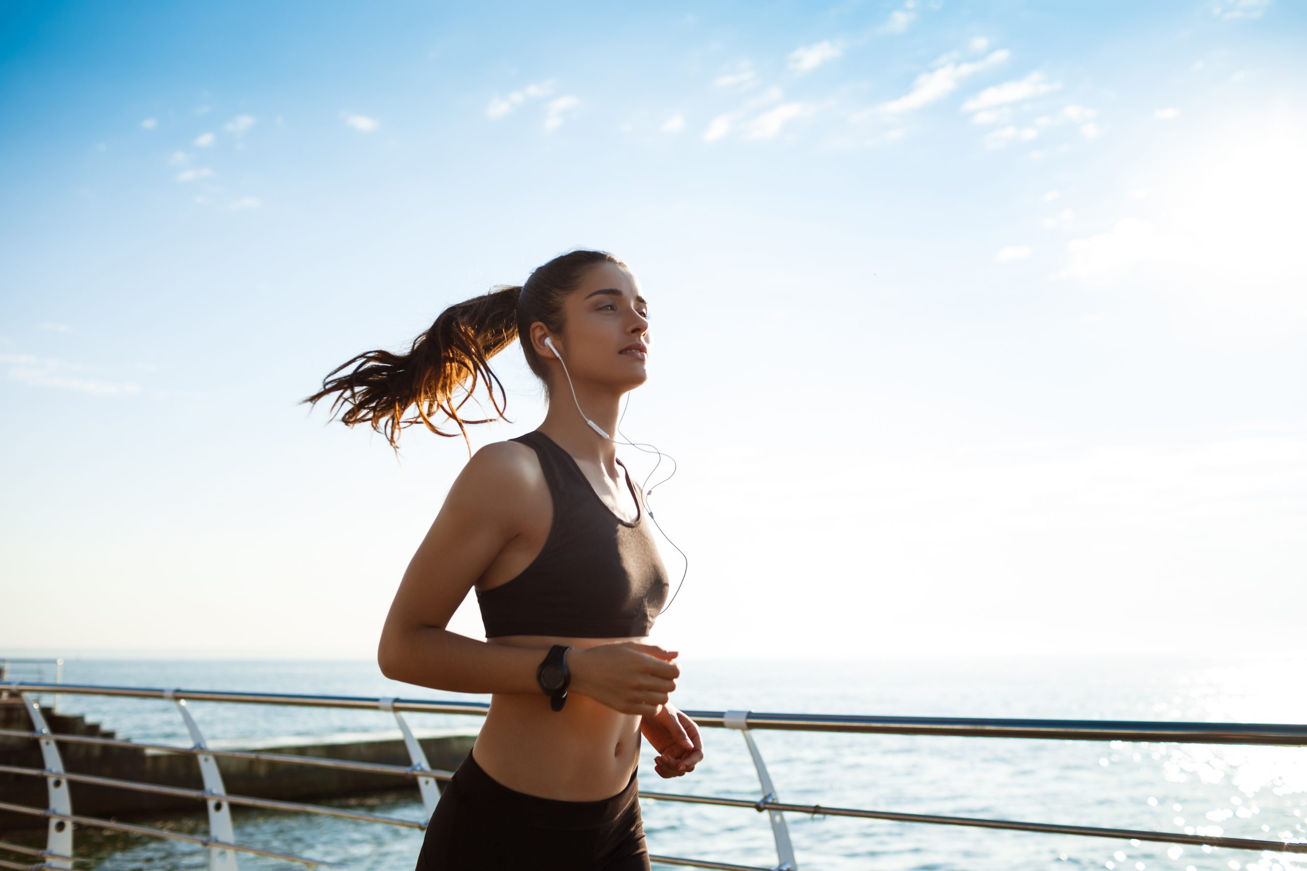 Woman jogging beside a waterfront in black athletic wear and earphones