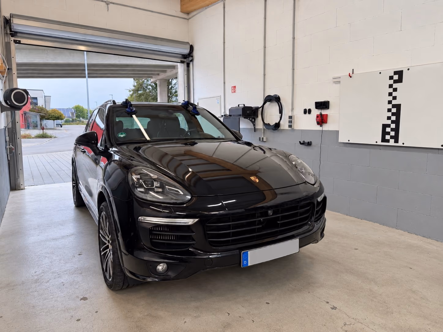 Porsche Cayenne mit neuer Frontscheibe in der Glastaxi-Werkstatt in Sandhausen, daneben die Kalibriertafel für die Fahrerassistenz