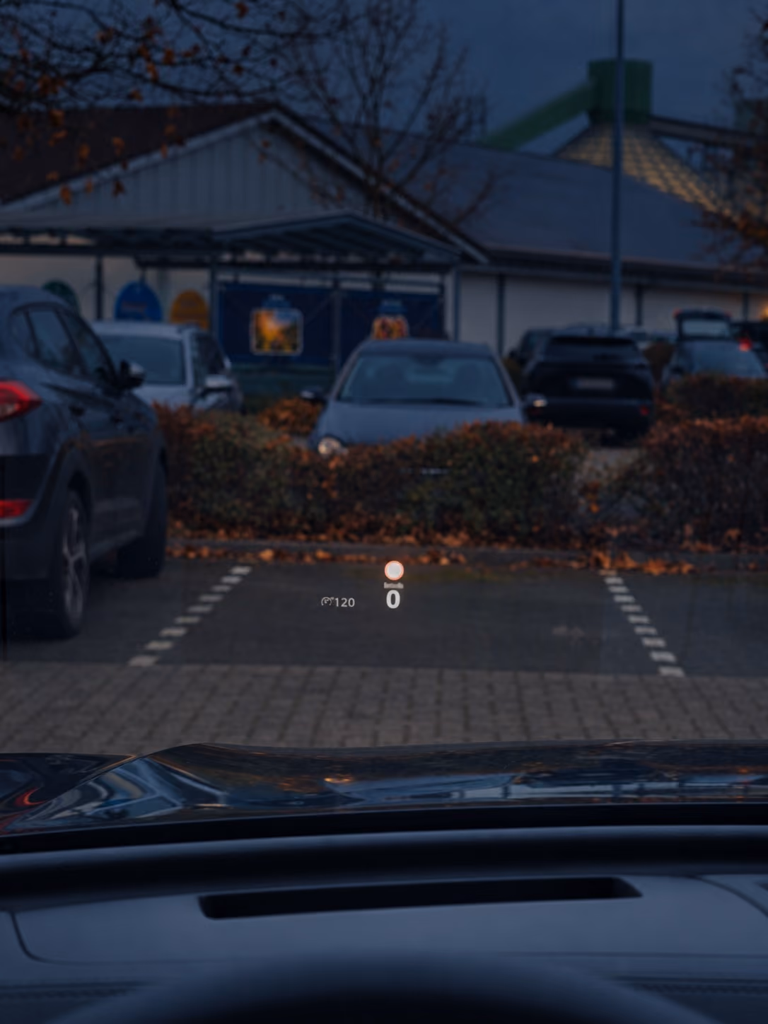 Head-up-Display spiegelt Geschwindigkeit und Tempolimit in die Frontscheibe, dahinter ein Parkplatz in der Dämmerung