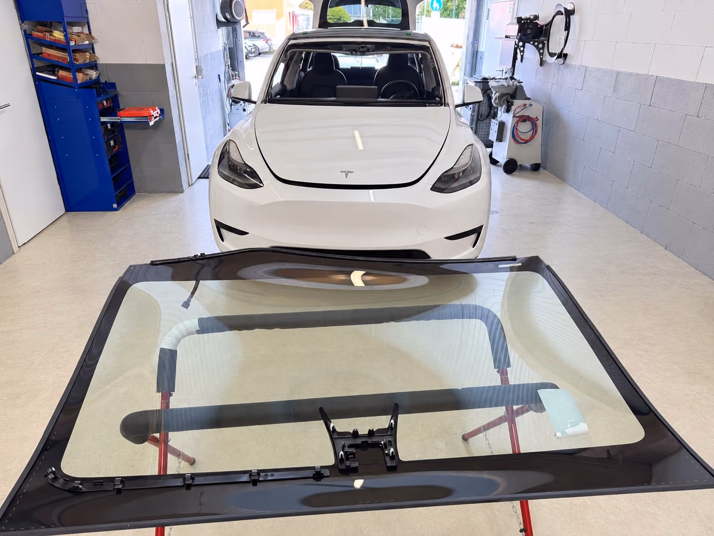 Neue Frontscheibe auf dem Montagebock in der Glastaxi-Werkstatt in Sandhausen, dahinter der Tesla, der sie bekommt