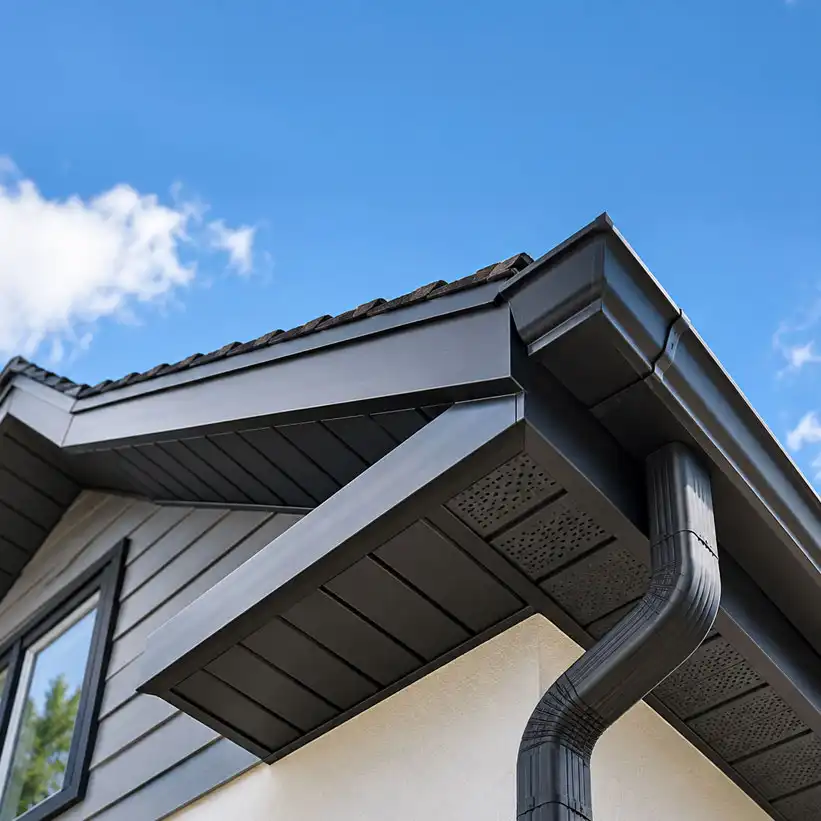 Close-up of brick house roofline with white soffits, fascia boards, and black guttering with downpipes against a blue sky