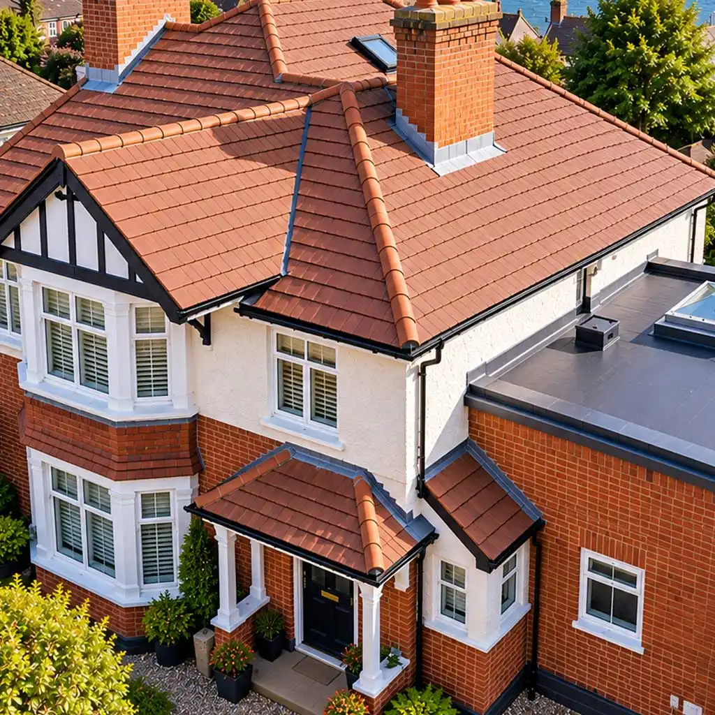 High-angle aerial view of a fully renovated Portsmouth home with perfectly aligned new tiled roof, clean flat roof extension, chimneys, and coastal harbor in the background.