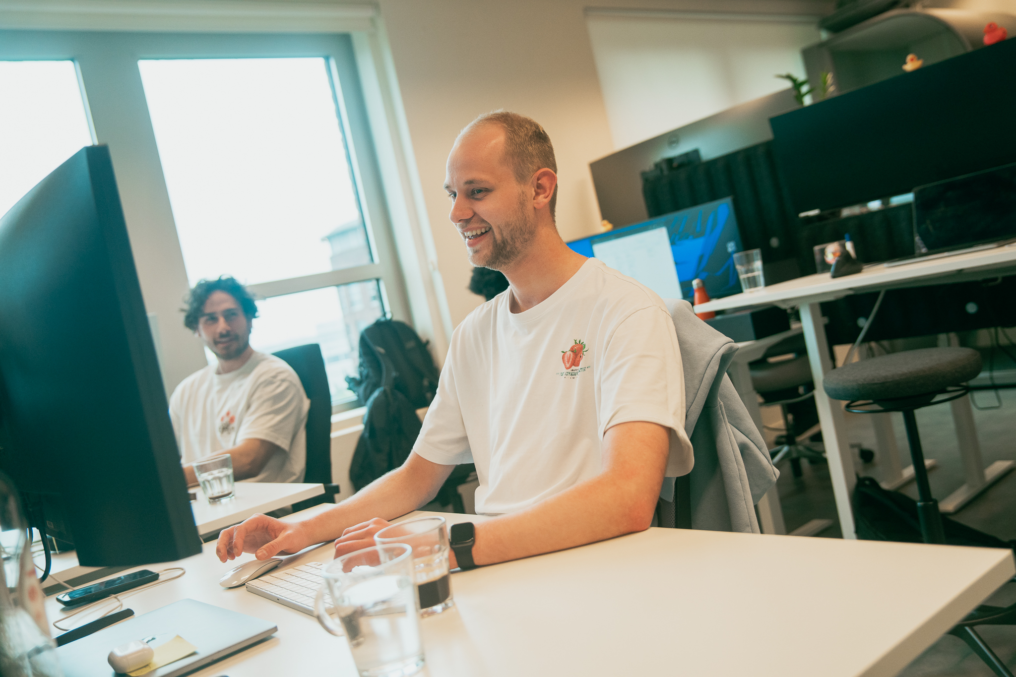 Twee mannen in witte overhemden die achter computers zitten in een lichte, moderne kantoorruimte.