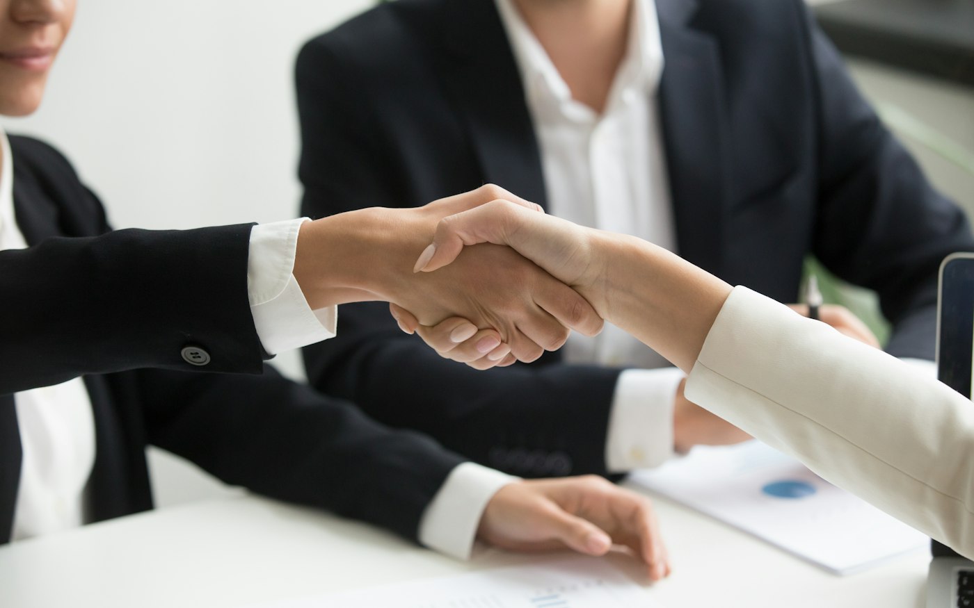 Two people shaking hands across a meeting table