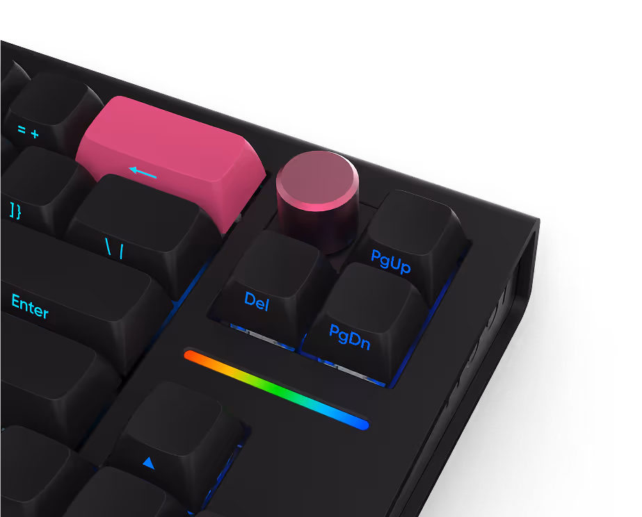 Close-up of black mechanical keyboard with a bright pink Enter key and volume control knob above Delete, Page Up, and Page Down keys, with a rainbow-colored LED strip below.