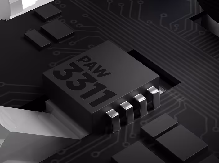 Close-up of a black electronic chip labeled PAW 5311 on a circuit board with metallic connectors.