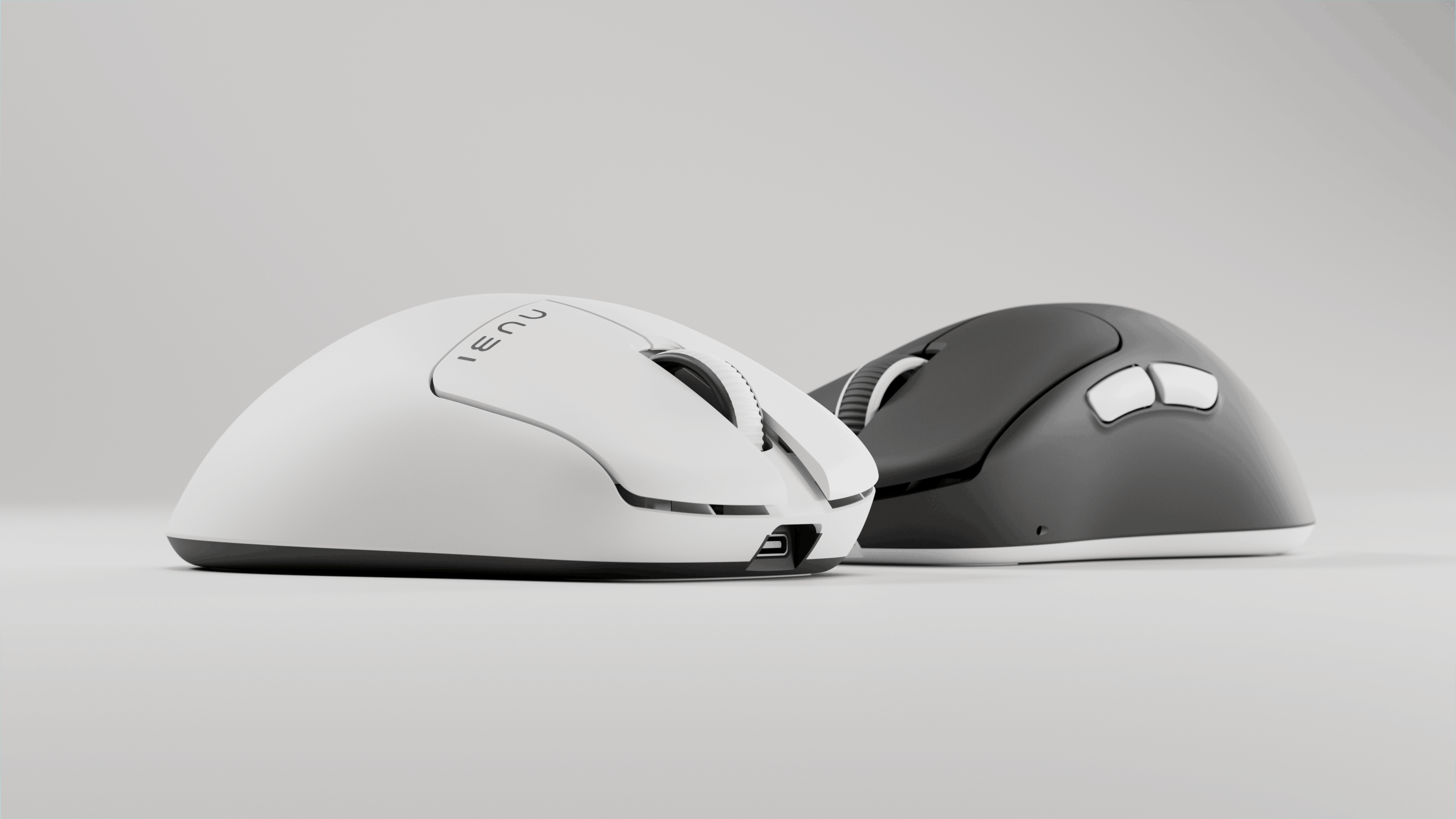 Two computer mice on a white surface, one white with a USB-C port visible at the front and the other black with two side buttons and a scroll wheel.