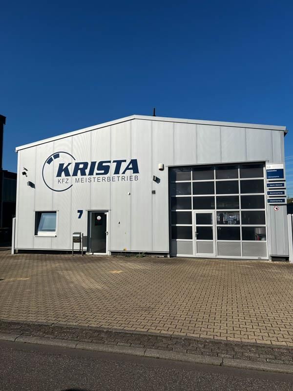 Frontale Außenansicht eines weißen Gebäudes vor blauem Himmel mit der Aufschrift "Krista KFZ Meisterbetrieb"