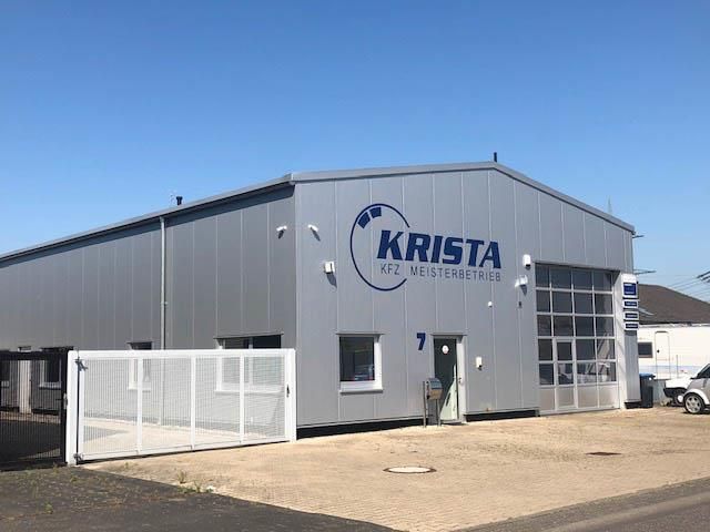 Außenansicht eines weißen Gebäudes vor blauem Himmel mit der Aufschrift "Krista KFZ Meisterbetrieb"