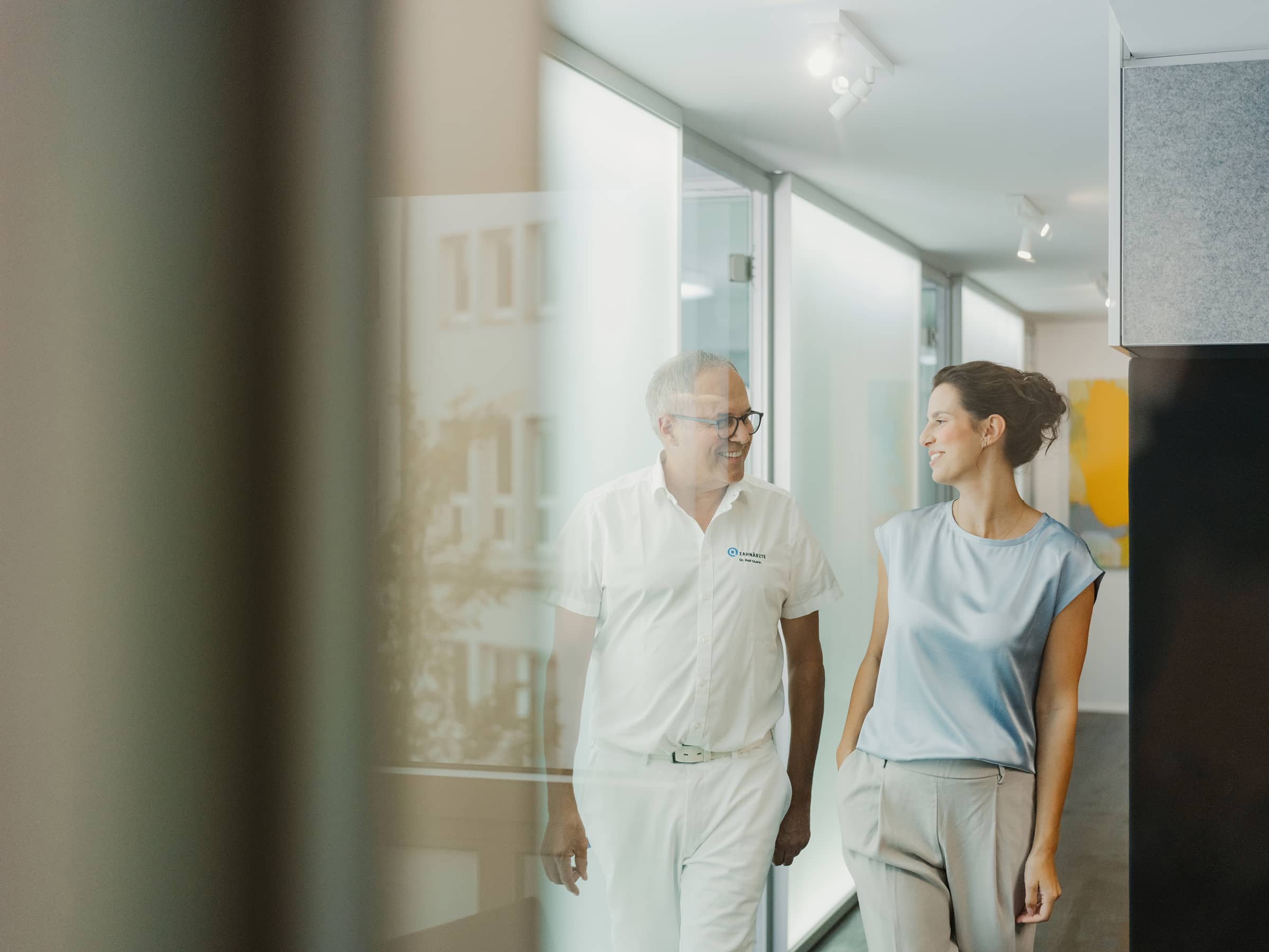 Zahnarzt und Patientin im persönlichen Gespräch auf dem Flur – transparente Beratung und individuelle Ästhetikplanung mit Digital Smile Design bei den Q-Zahnärzten Freiburg.