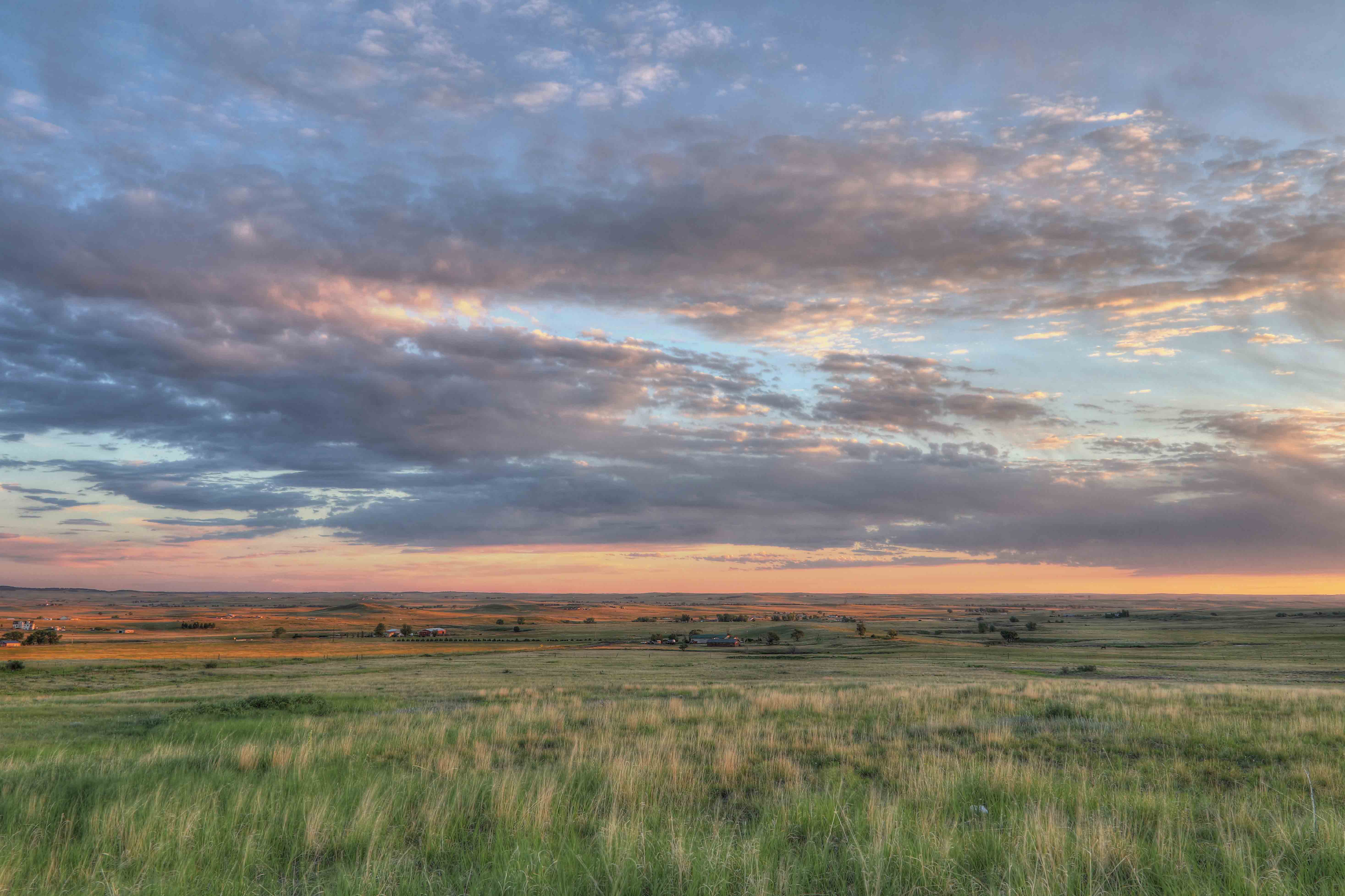 Open grassy fields under a colorful sunset sky with scattered clouds.