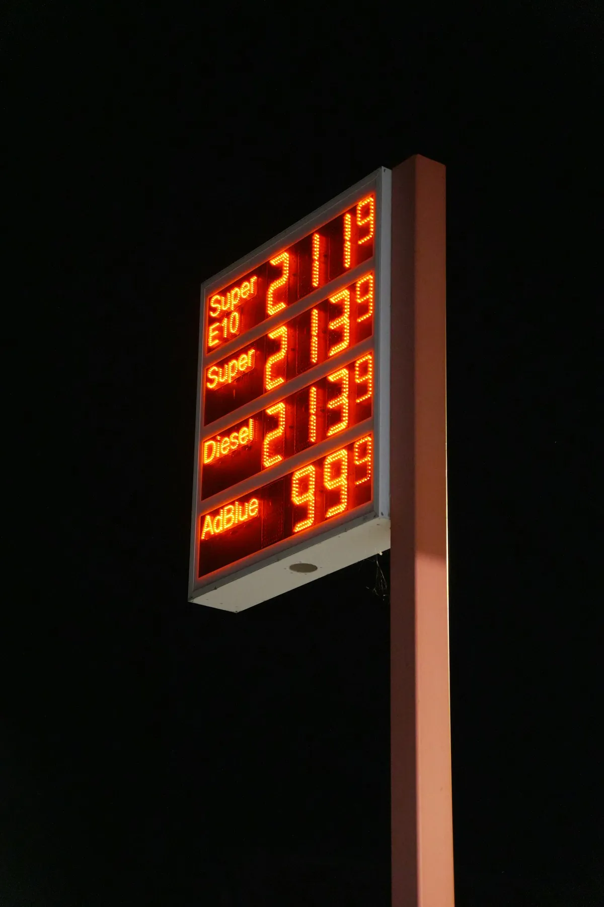 A glowing red digital fuel price sign standing against a dark night sky