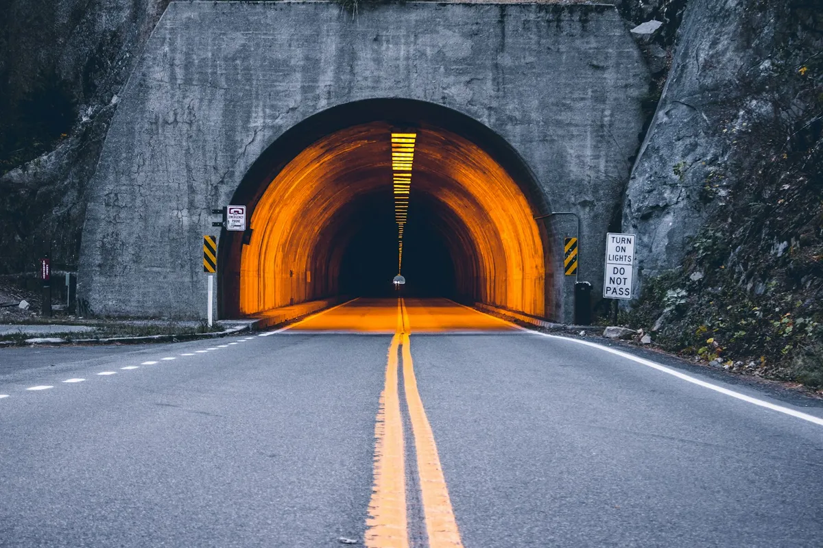 A road tunnel lit by a repeating run of yellow lights along its arch