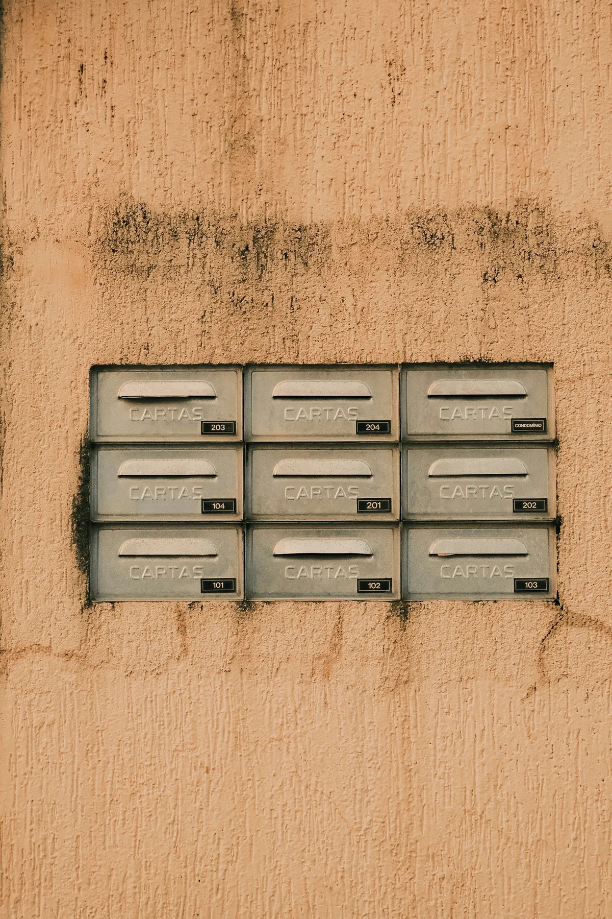 Nine metal mailboxes labelled CARTAS set in a grid into a beige stucco wall