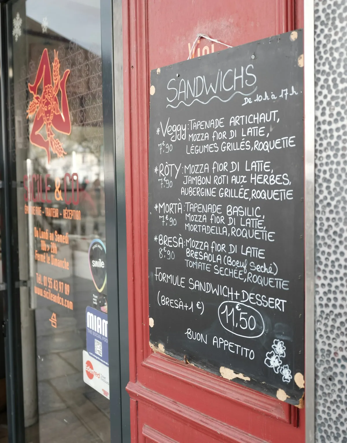 A chalkboard menu listing sandwiches with their prices written by hand
