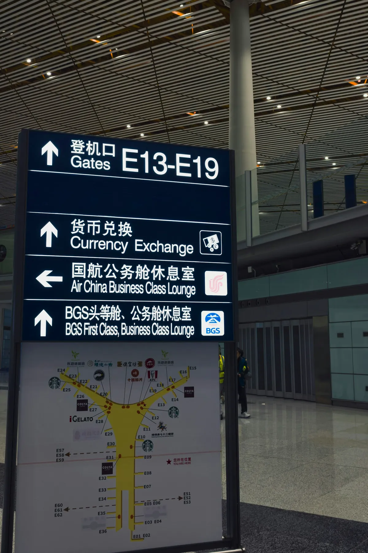 Airport sign stack listing gates, currency exchange and lounges with directional arrows