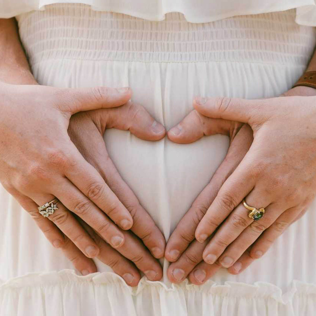 A view of a pregnant woman's belly are with her and her partner's hands forming a heart shape.