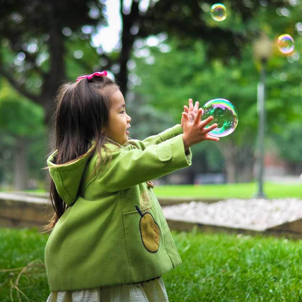 A child chases bubbles around a park, as you do. It looks like she can't catch them, but she seems determined.