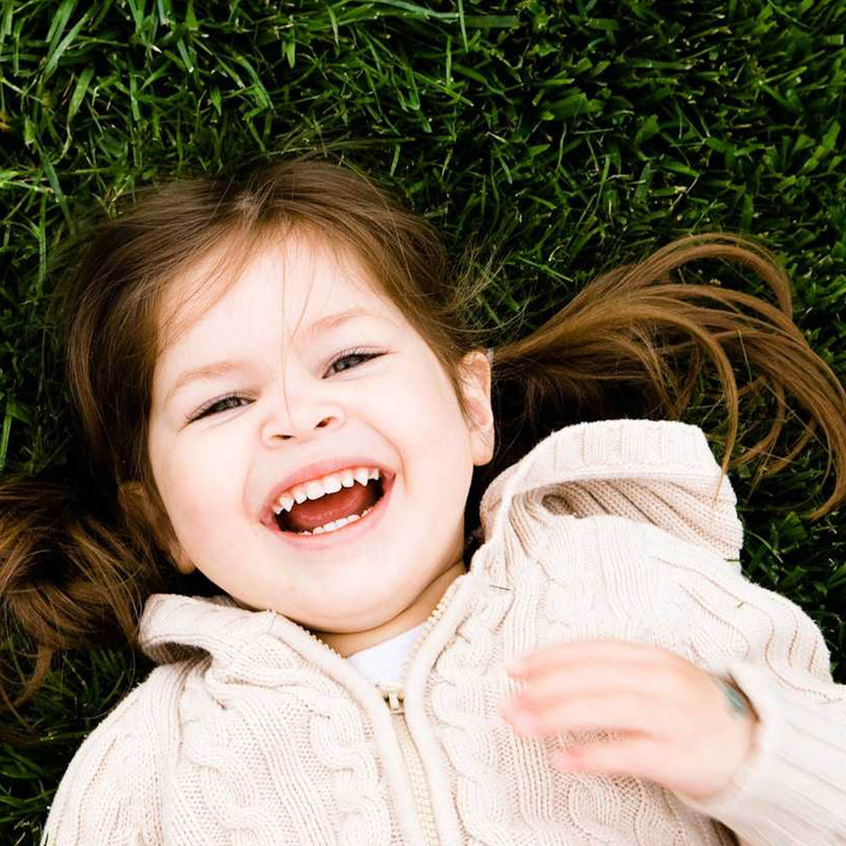 A young girl is looking up at the camera and laughing. She looks super happy to be laying in a field on such a nice day.