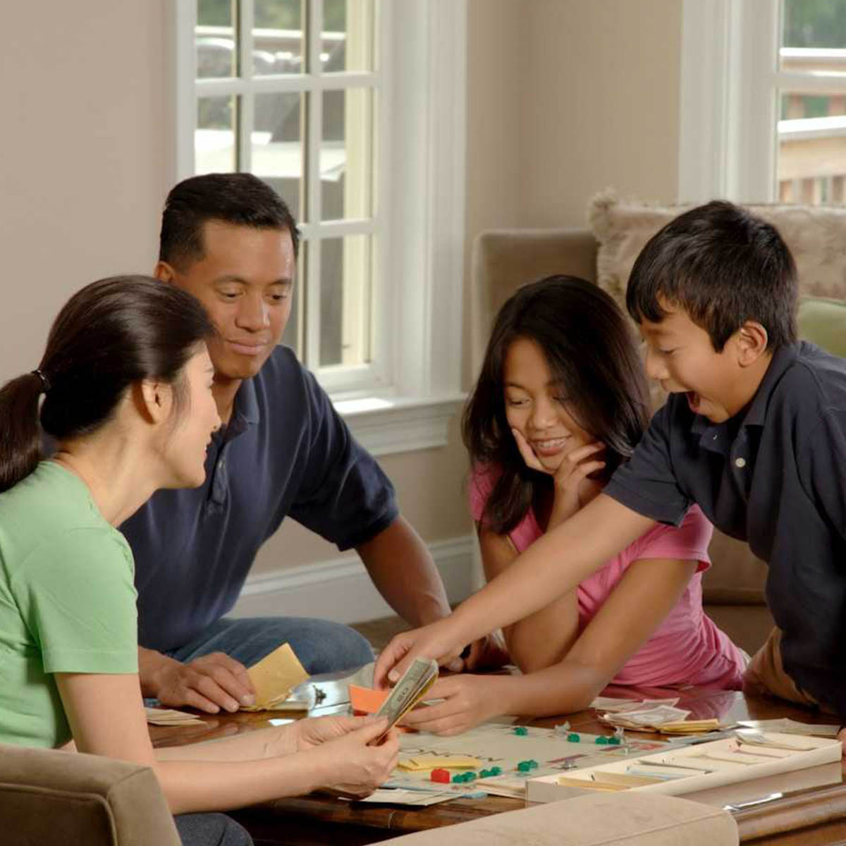 An Asian family is playing board games in a bright room. It looks like a young boy is winning.