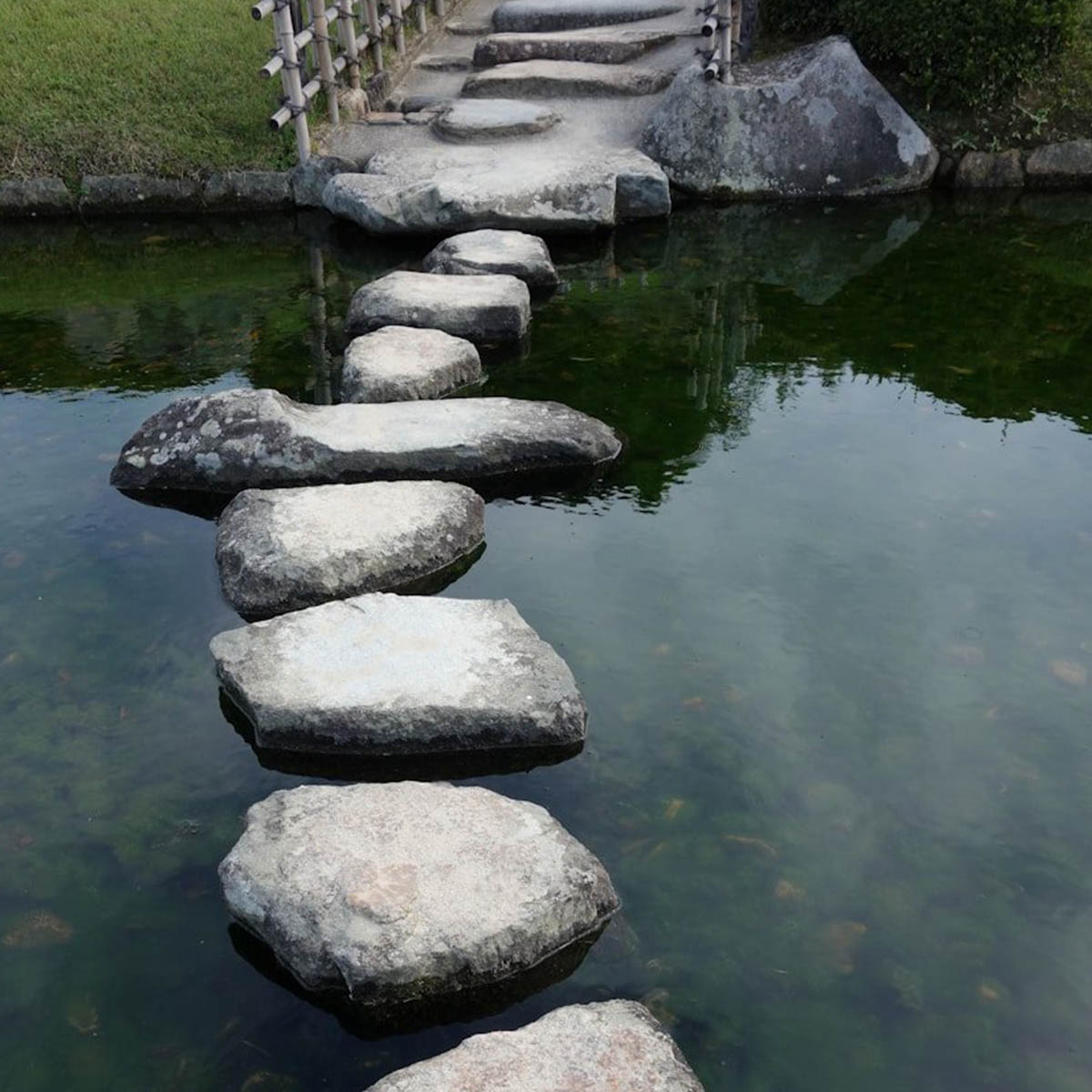 A calm stream with some stepping stones running up to a small bridge, suggesting tranquility and serenity.