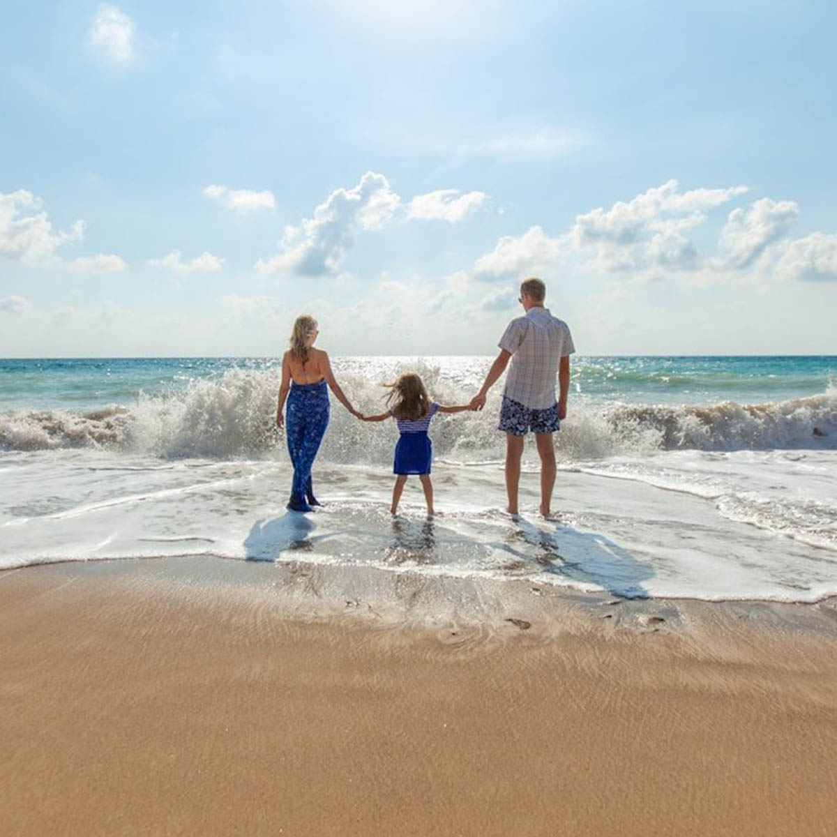 A family takes their young child to the shoreline as waves come in. It's a nice sunny day and looks like fun.