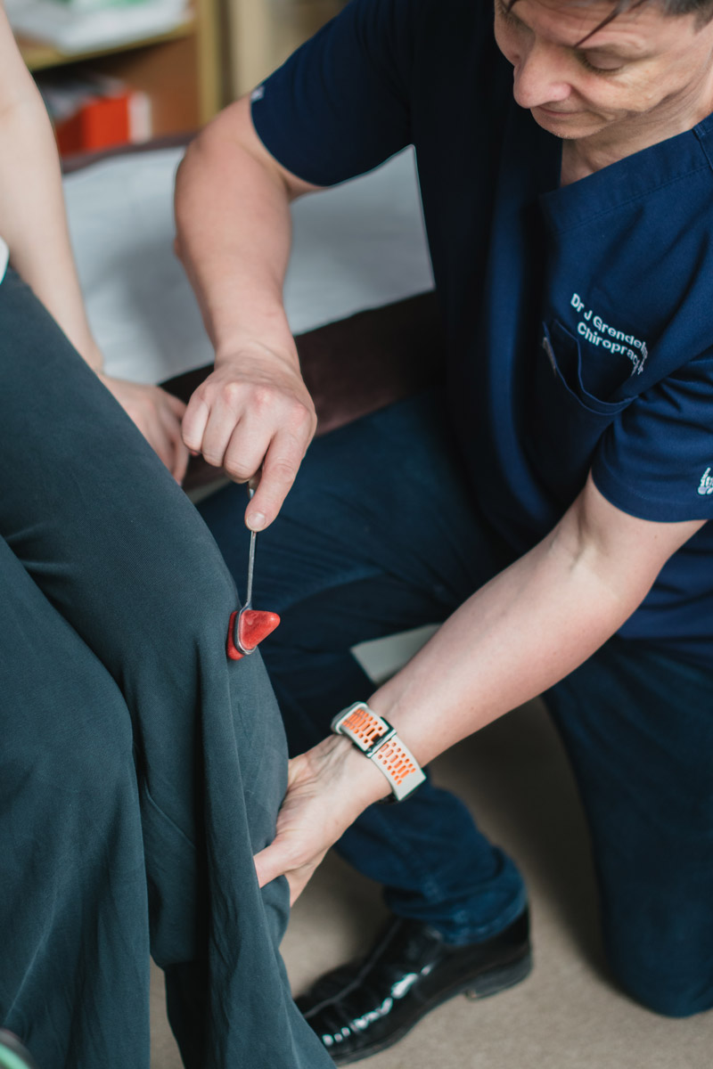A doctor testing knee reflex using a small medical tool.